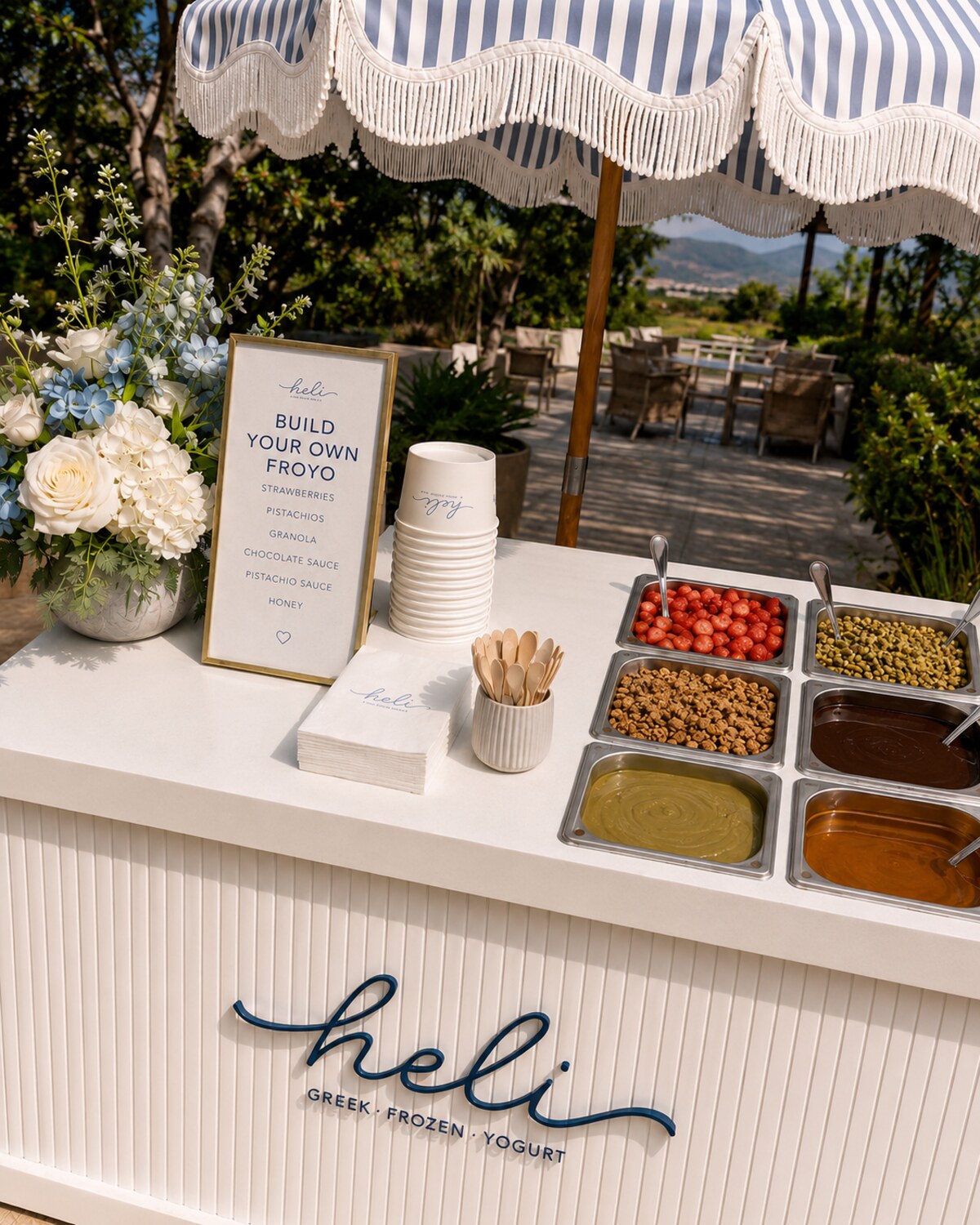 Close view of the Heli cart showing its striped umbrella, floral arrangement, branded menu, cups, topping bar, and logo